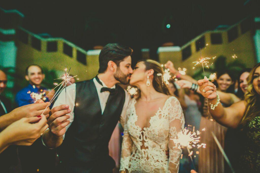 Bride and groom share a romantic kiss surrounded by sparklers at a wedding celebration.