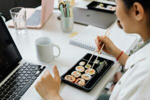 Person having sushi with chopsticks at a desk, blending work and dining.